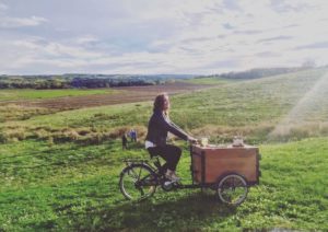 woman riding a custom stained cedar ice cream bike in the fields of Halifax on a sunny day