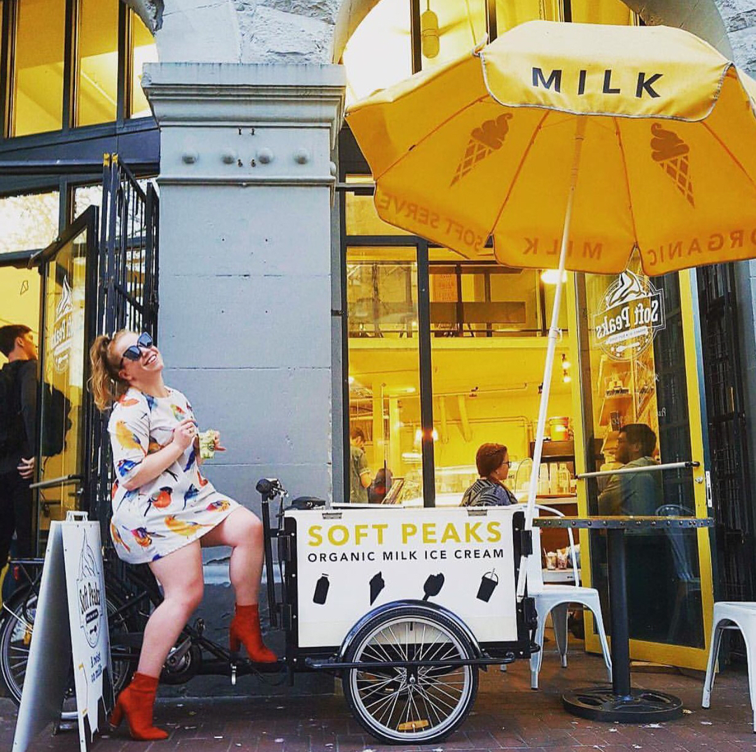 Girl enjoying treat sitting on Soft Peaks Ice Cream Bike with umbrella out front of Ice Cream shop in Vancouver British Columbia